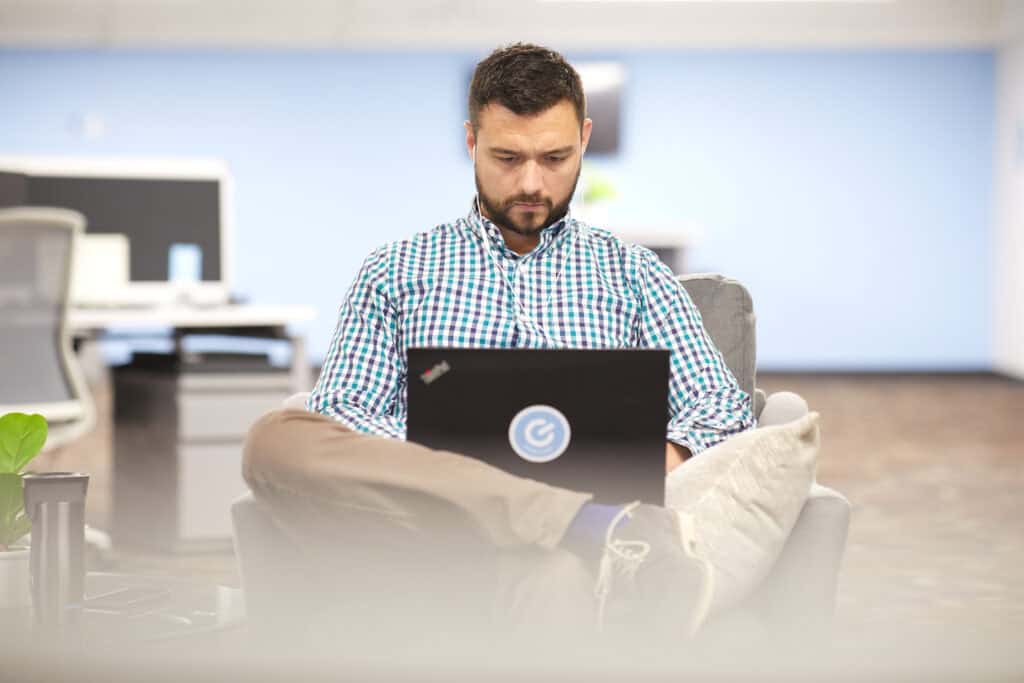 A photo of a team member looking down at an open laptop computer on his lap.